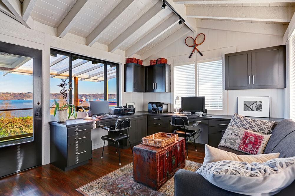 Coastal home office with dark cabinetry, dual desks, and waterfront views
